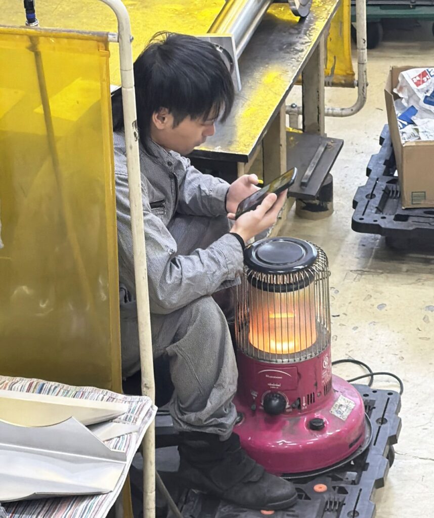 工場内でストーブに当たる従業員